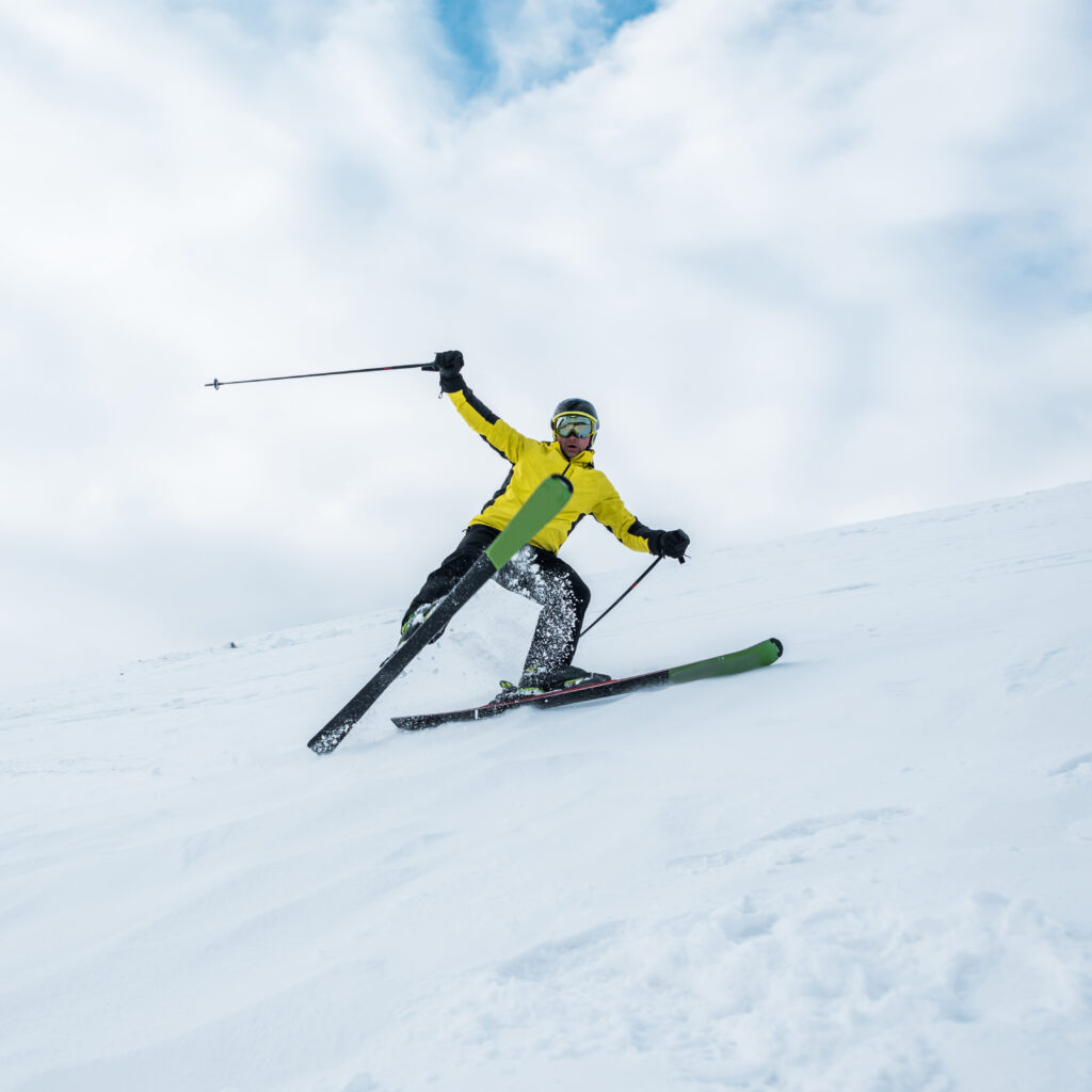 Skier in bright yellow jacket carving down snowy slope, representing winter apparel care by Sudsies.