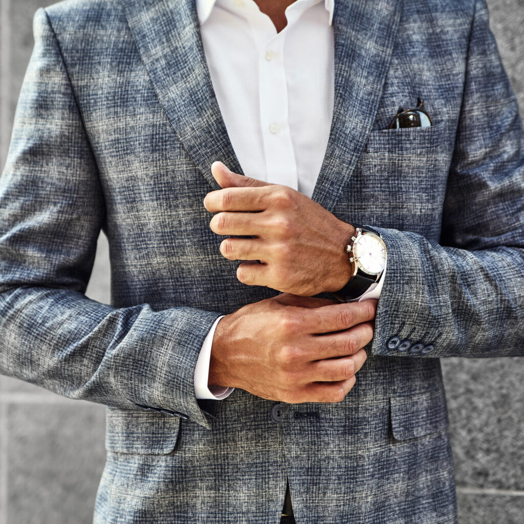 Close-up of a well-dressed man in a tailored blue plaid suit adjusting his cuffs, illustrating luxury garment care and suit history.