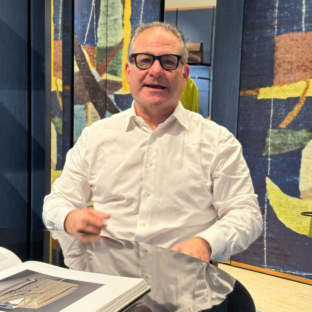 Jason Loeb seated indoors wearing a white shirt and glasses, reviewing fabric materials