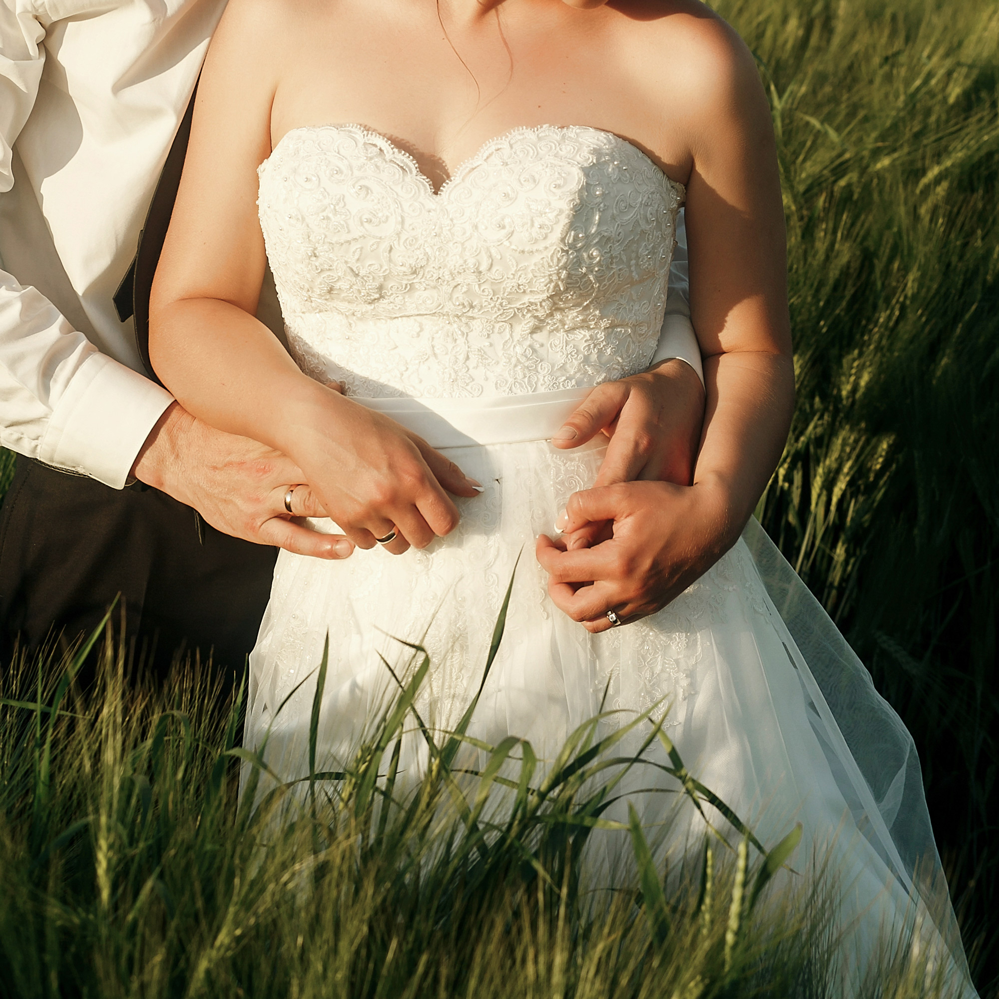 Bride and groom standing together in a field with hands resting on a wedding gown