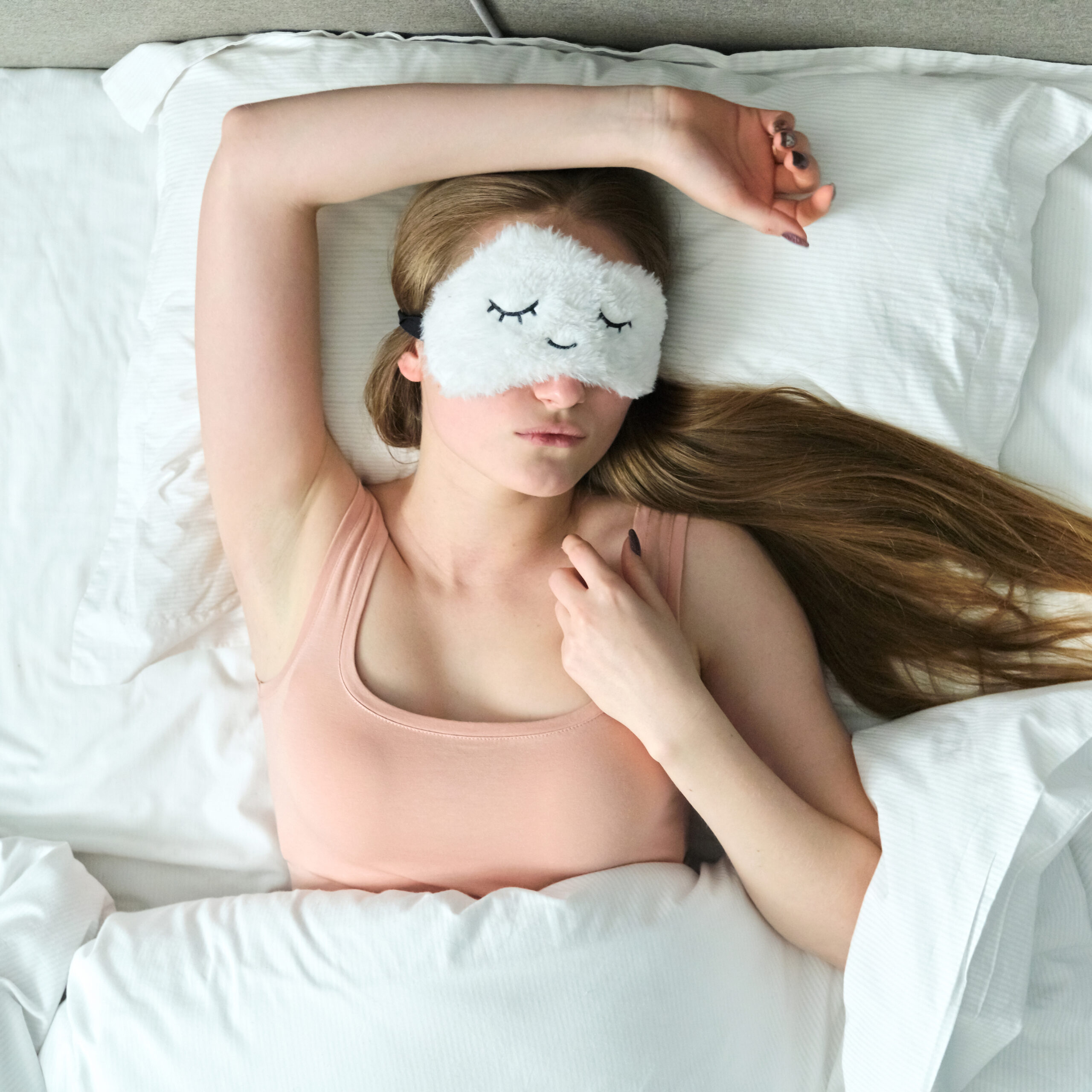 Woman sleeping peacefully in bed with fluffy sleep mask and high-quality white sheets