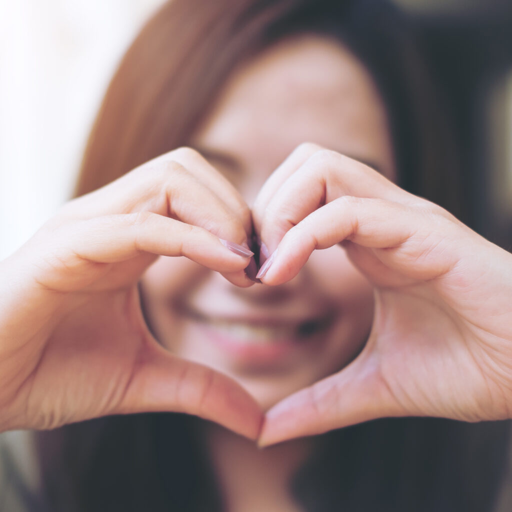 Smiling woman making heart hand gesture – representing the Sudsies Smile and exceptional dry cleaning service in Bal Harbour, Edgewater, Fisher Island, and across South Florida