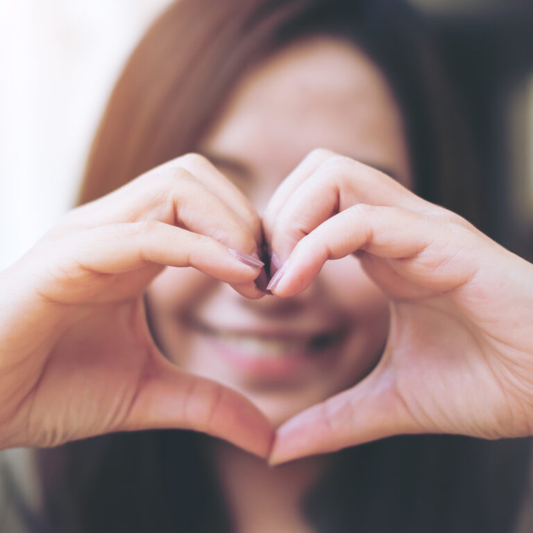 Smiling woman making heart hand gesture – representing the Sudsies Smile and exceptional dry cleaning service in Bal Harbour, Edgewater, Fisher Island, and across South Florida