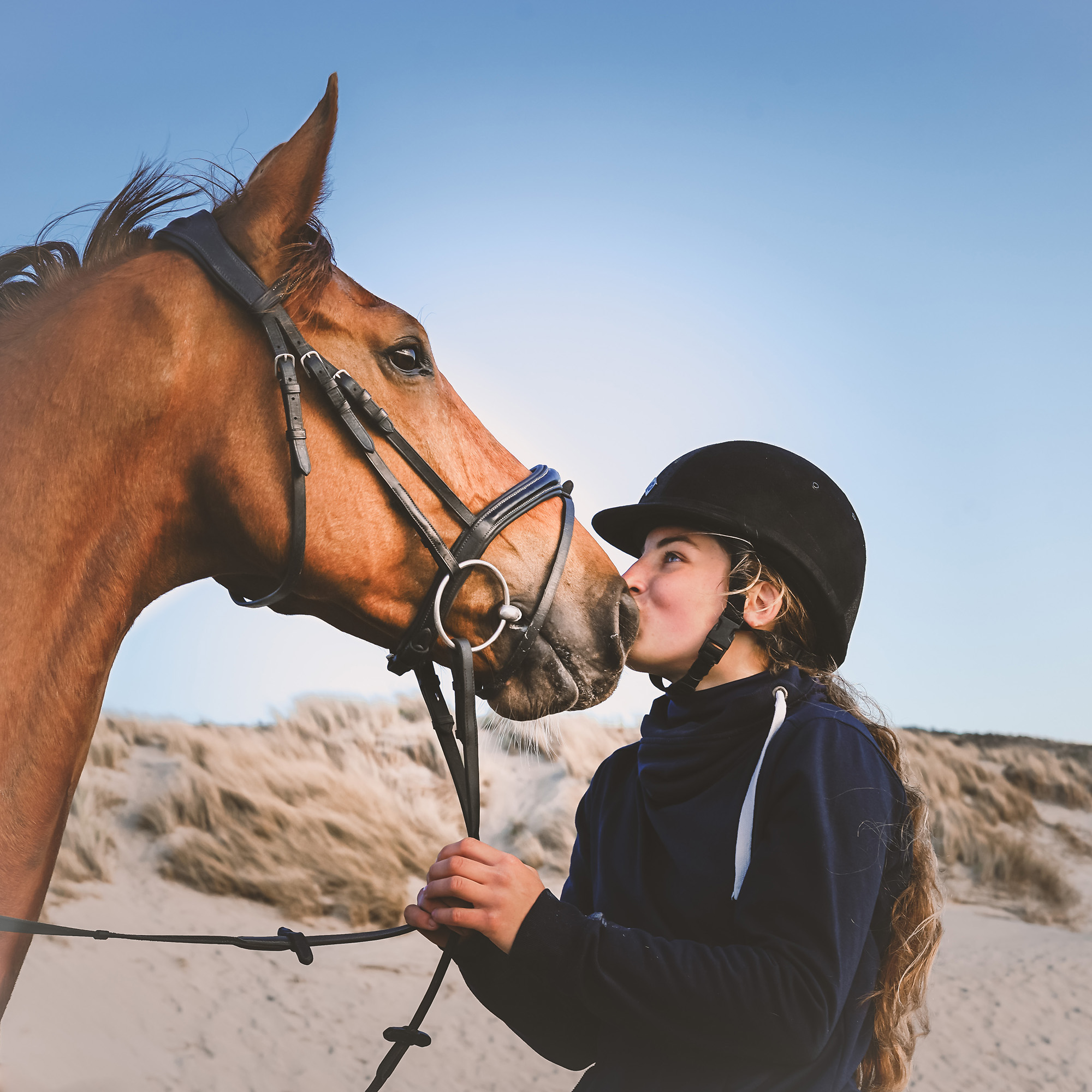 Young equestrian wearing a helmet standing beside a horse outdoors