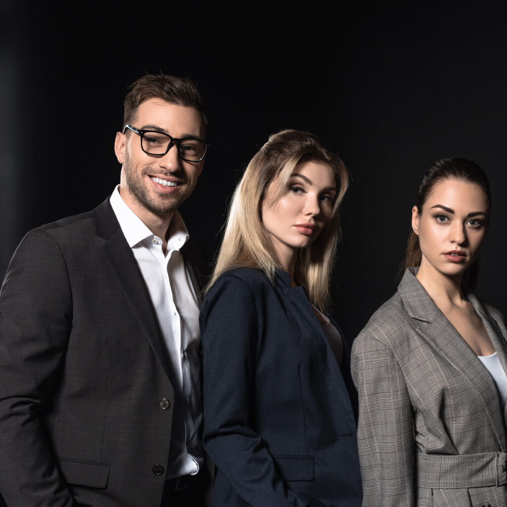 Three professionally dressed individuals in luxury suits and business attire standing confidently against a dark background—representing Sudsies’ expert dry cleaning services in Miami Beach, Fort Lauderdale, and Palm Beach.