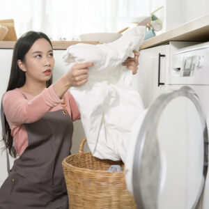 Young woman doing laundry and inspecting white garment before washing