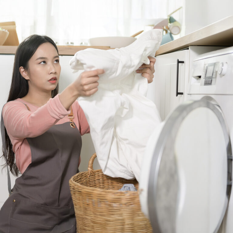Young woman doing laundry and inspecting white garment before washing