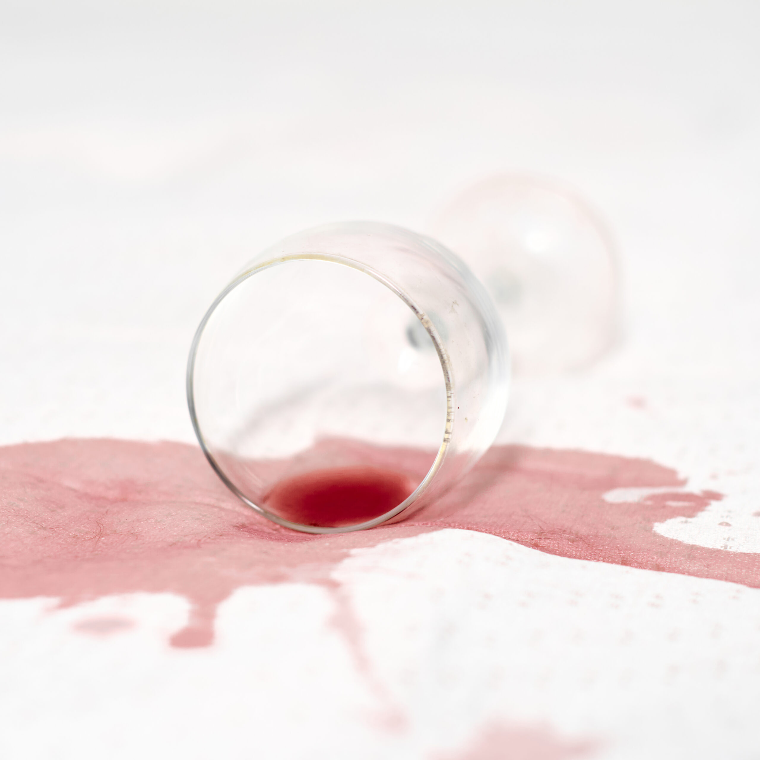 Red wine spilled on white fabric with an overturned wine glass