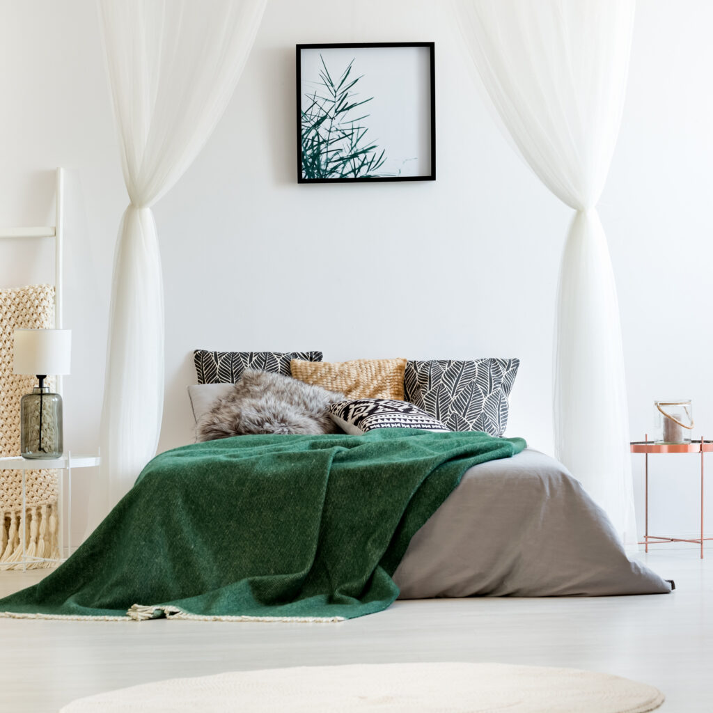 Minimalist bedroom featuring clean bedding with green wool throw, patterned pillows, and white canopy, illustrating Sudsies’ professional linen cleaning service for a healthy sleep environment.