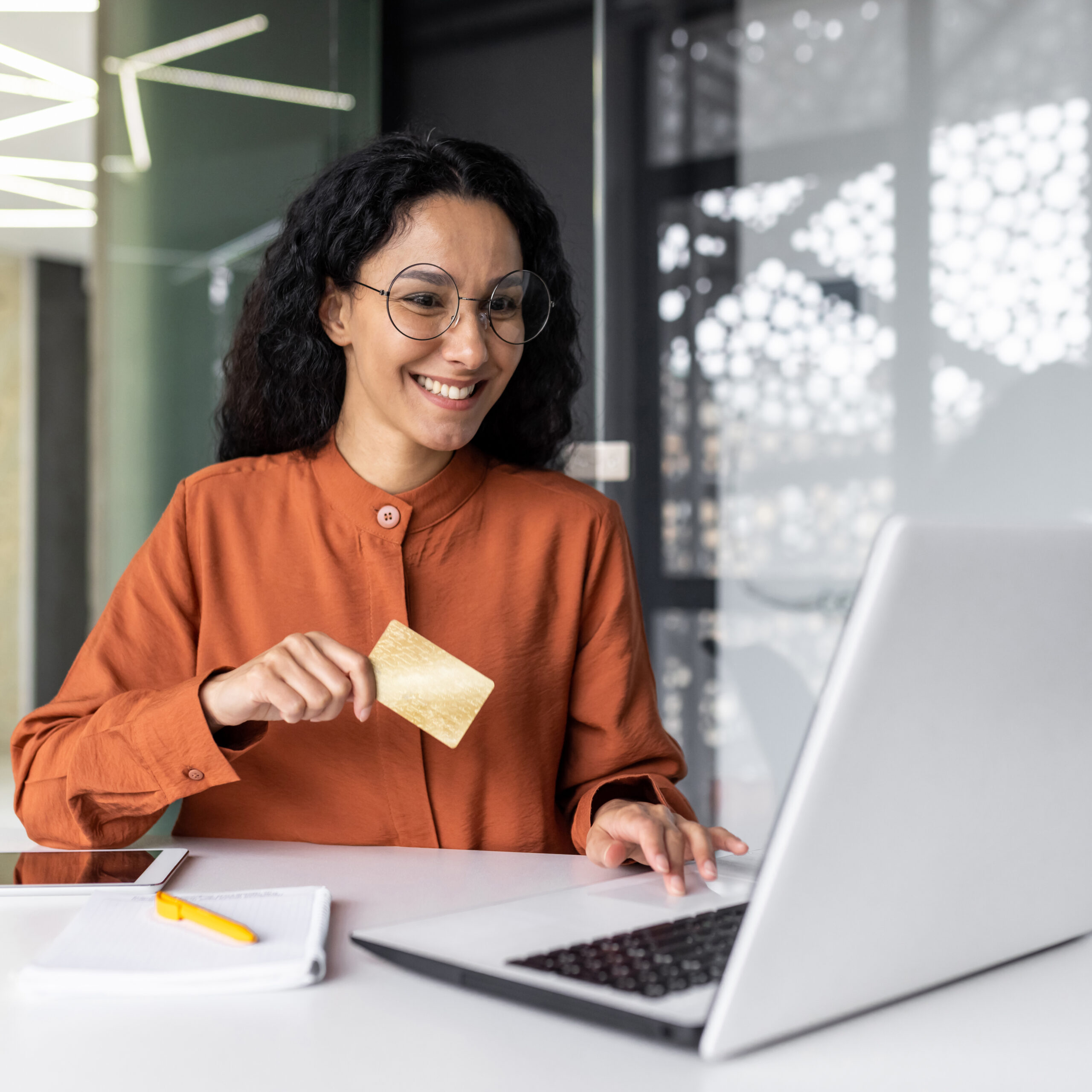 Smiling woman using a laptop and holding a gold credit card, representing Sudsies’ new easy-to-use online dry cleaning platform.