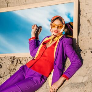 Woman leaning against house wearing sunglasses and designer clothing