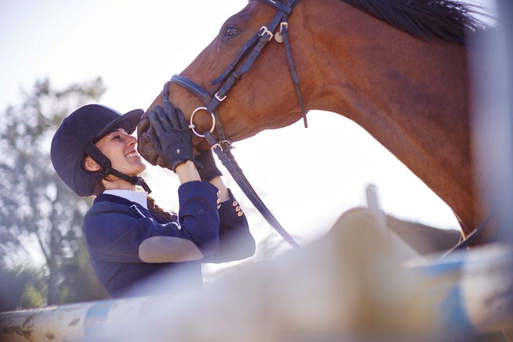 Smiling woman in equestrian clothing kisses her horse after exiting the show ring.