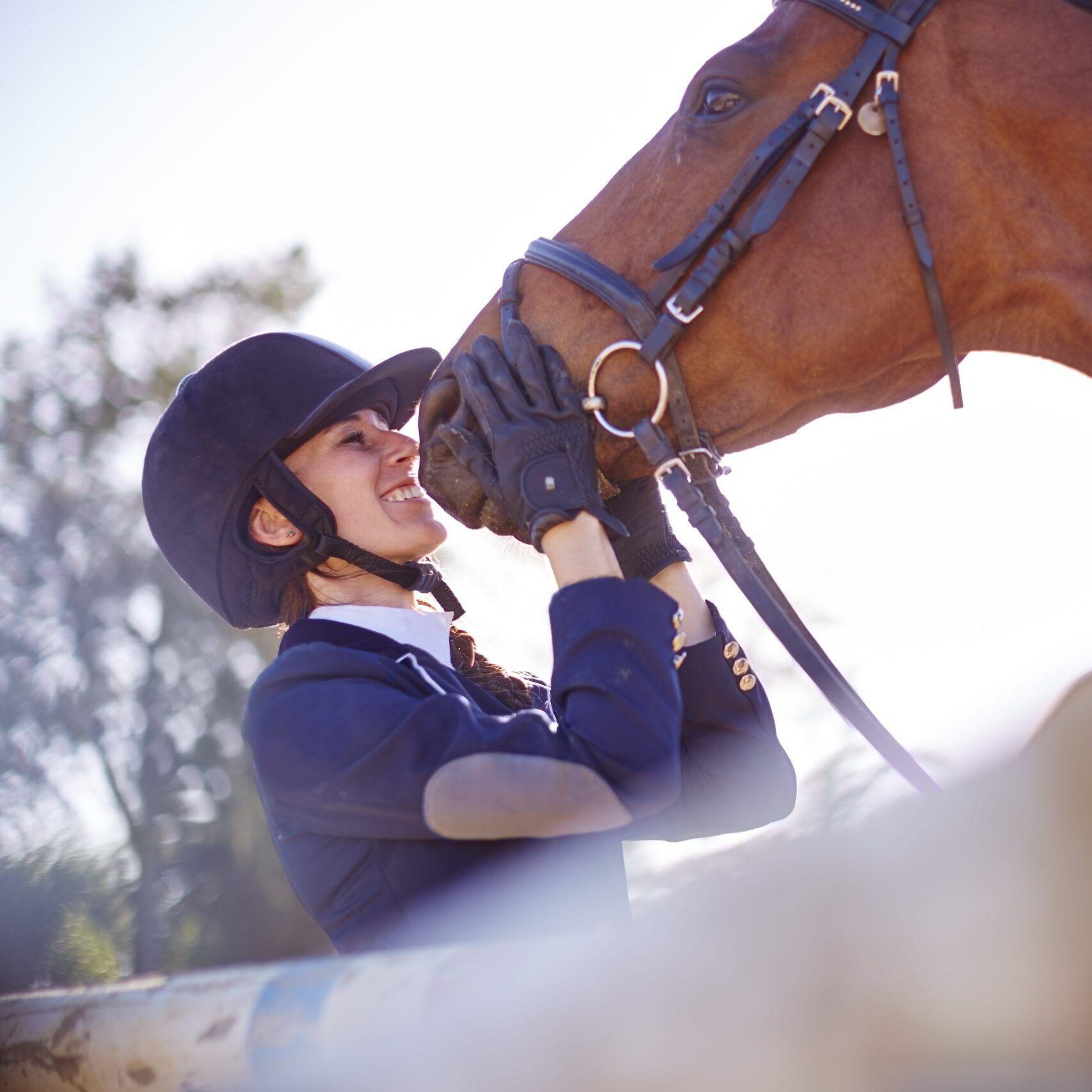 Smiling woman in equestrian clothing kisses her horse after exiting the show ring.