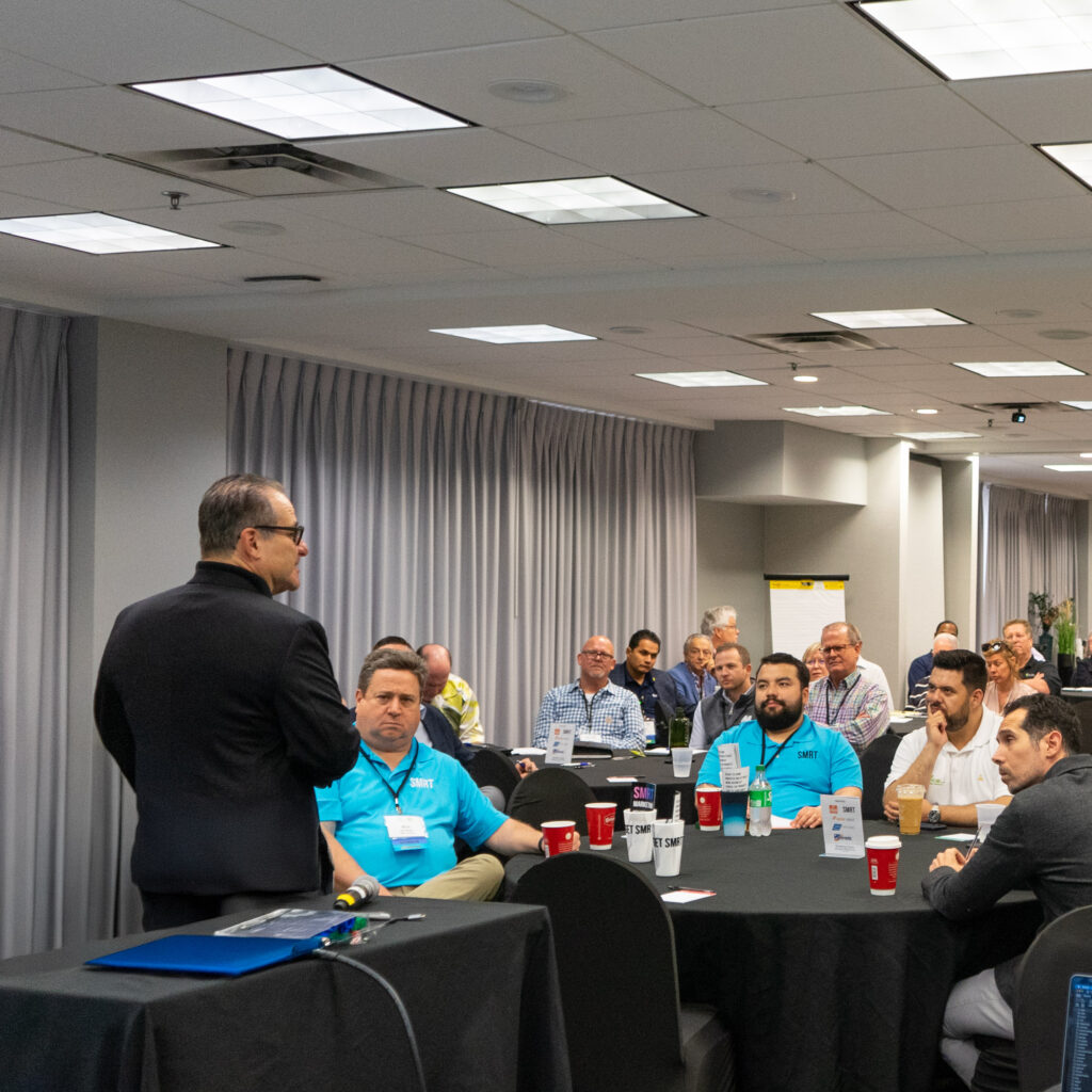 Industry professionals attending a dry cleaning conference seated at round tables during a presentation