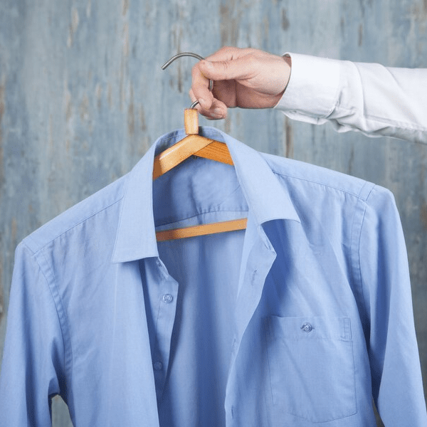 Hand holding a freshly cleaned light blue dress shirt on a wooden hanger