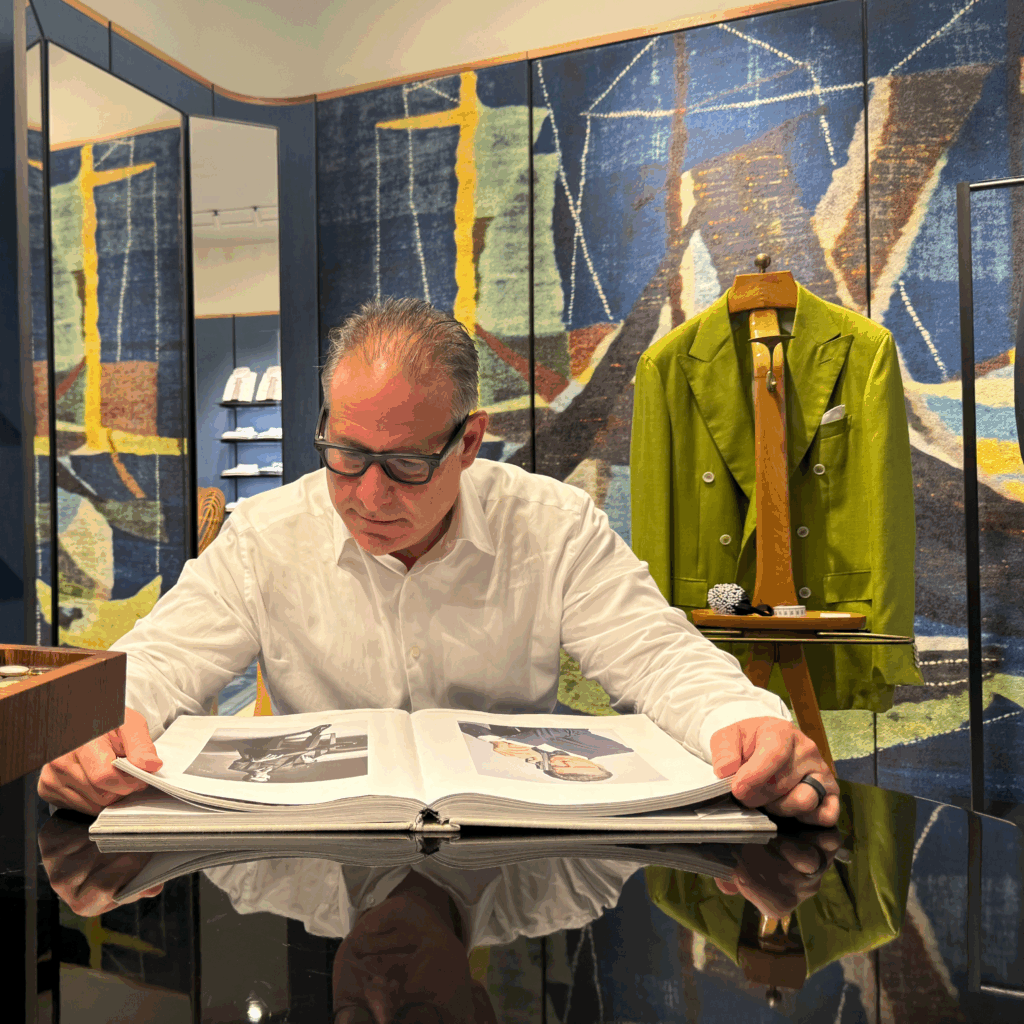 man examines book while a couture coat hangs behind him