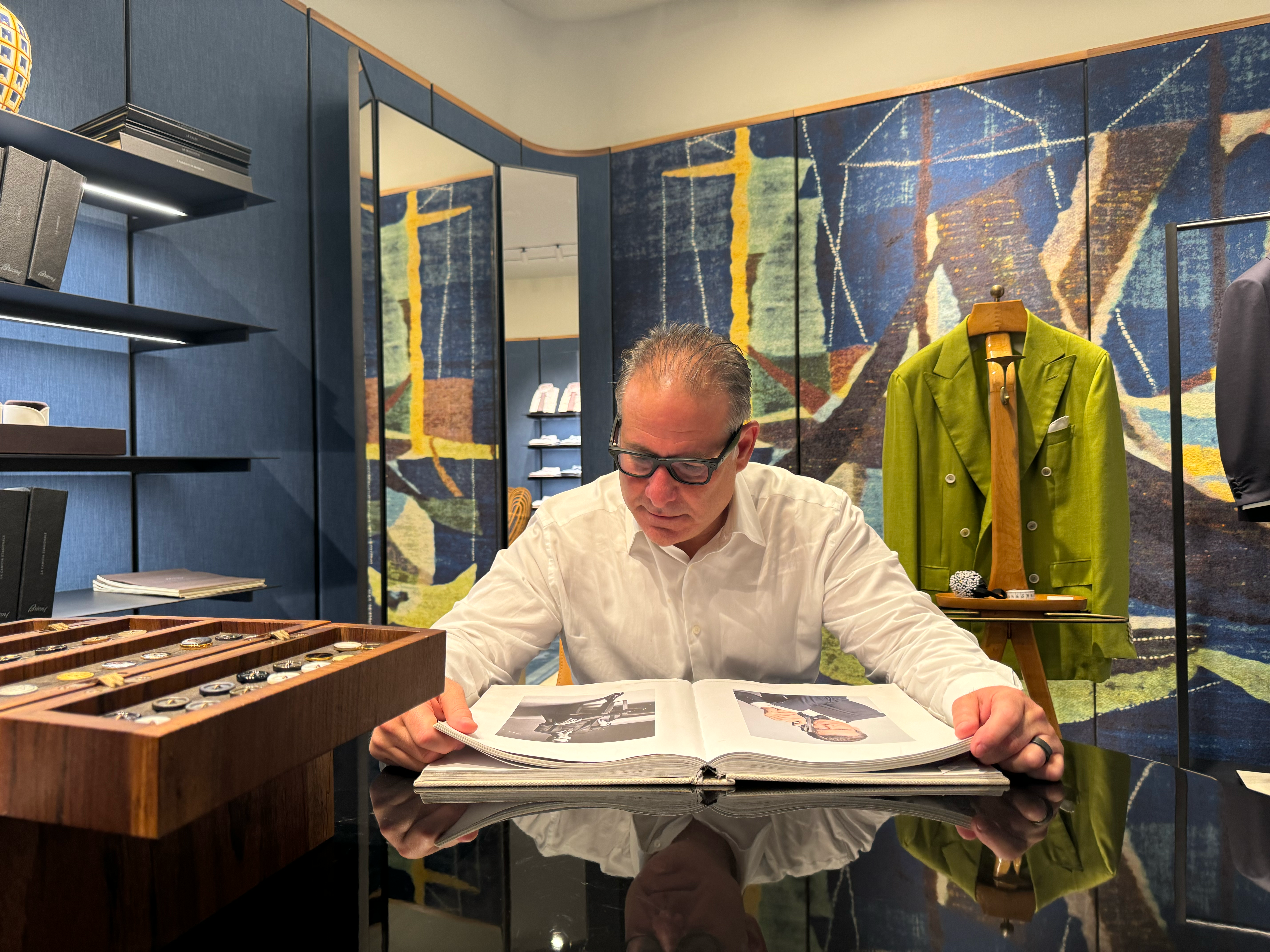 man examines book while a couture coat hangs behind him