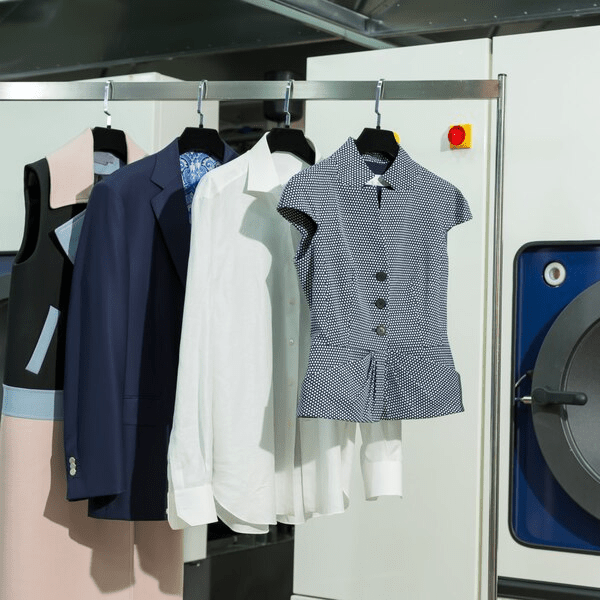 Freshly dry-cleaned garments hanging beside a modern dry cleaning machine