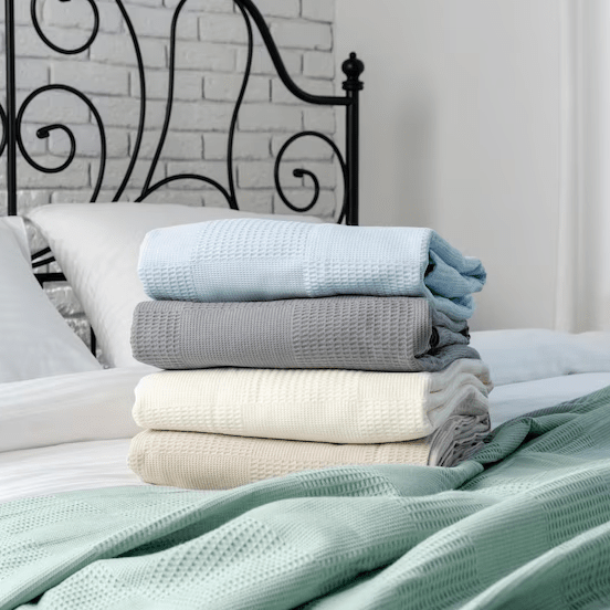 Neatly folded bedroom linens stacked on a white bed with a wrought iron headboard