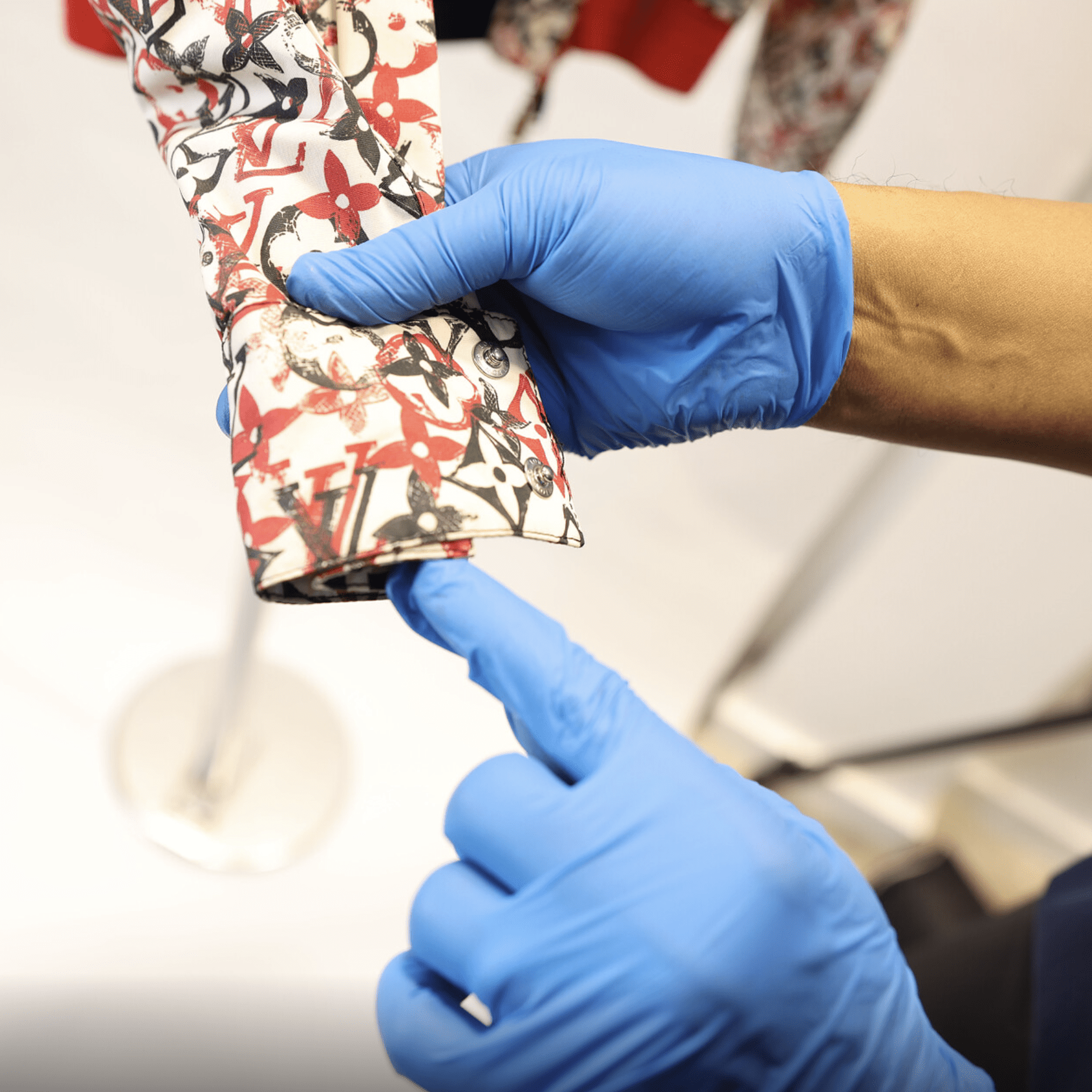 Gloved hands inspect mold damage on a Louis Vuitton designer garment at Sudsies