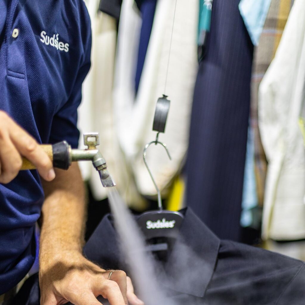 Sudsies team member spot cleaning a black shirt in dry cleaning facility
