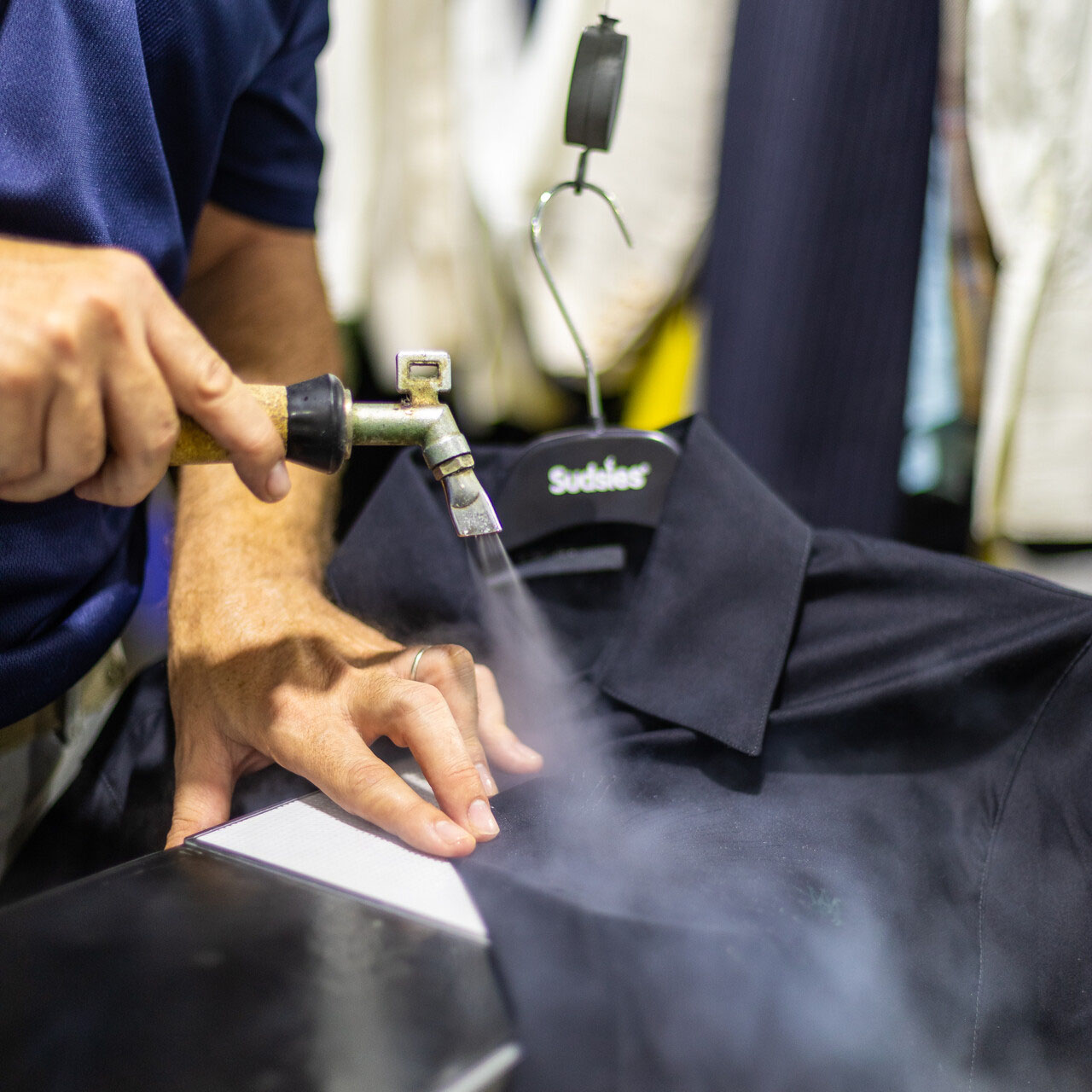Sudsies team member spot cleaning a black shirt in dry cleaning facility