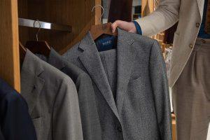 A person selects a Mond gray suit jacket from a refined wooden closet