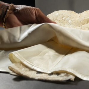 Detail of a hand carefully holding a century-old lace and silk dress for preservation.