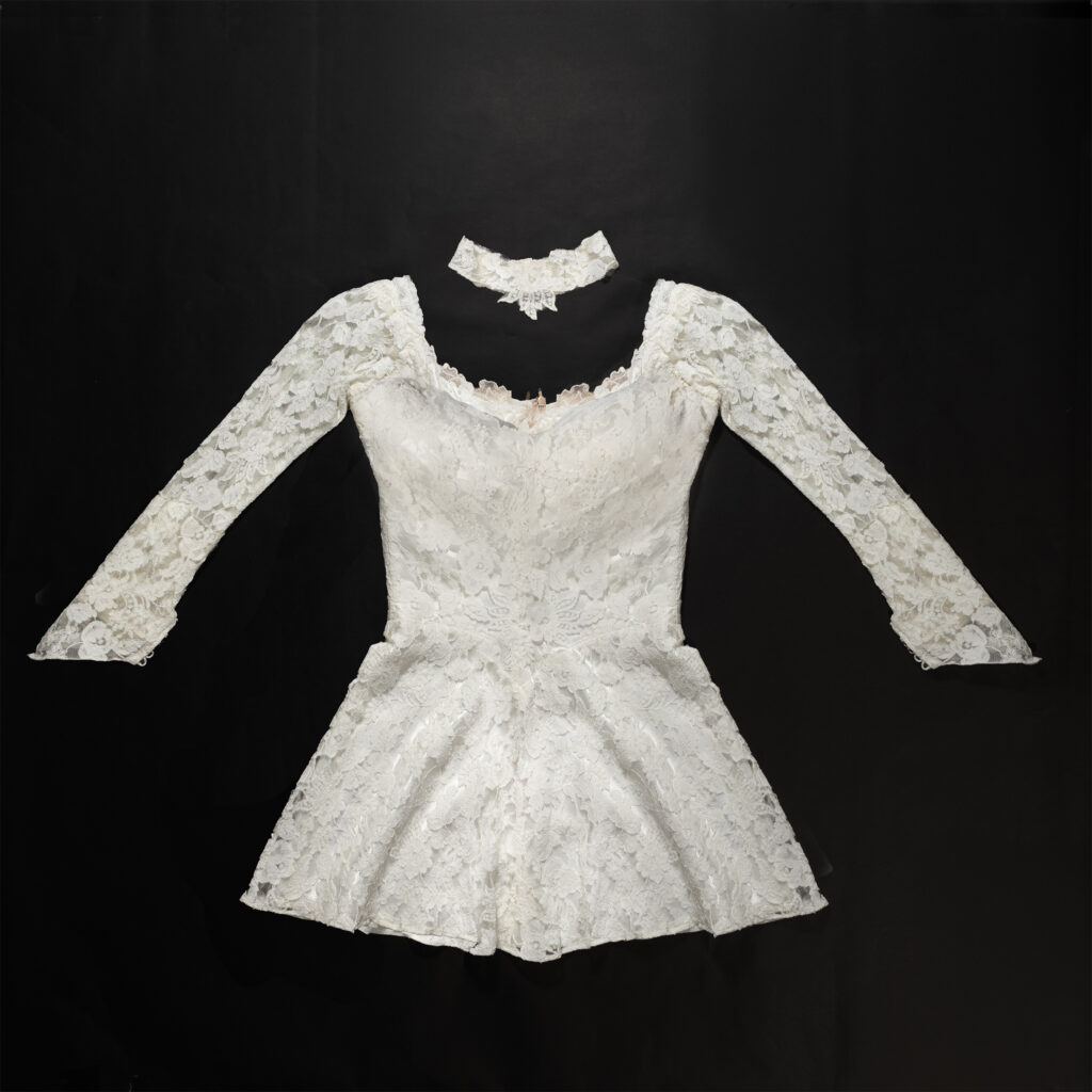Restored 73-year-old lace wedding dress with matching lace choker, laid flat on black background