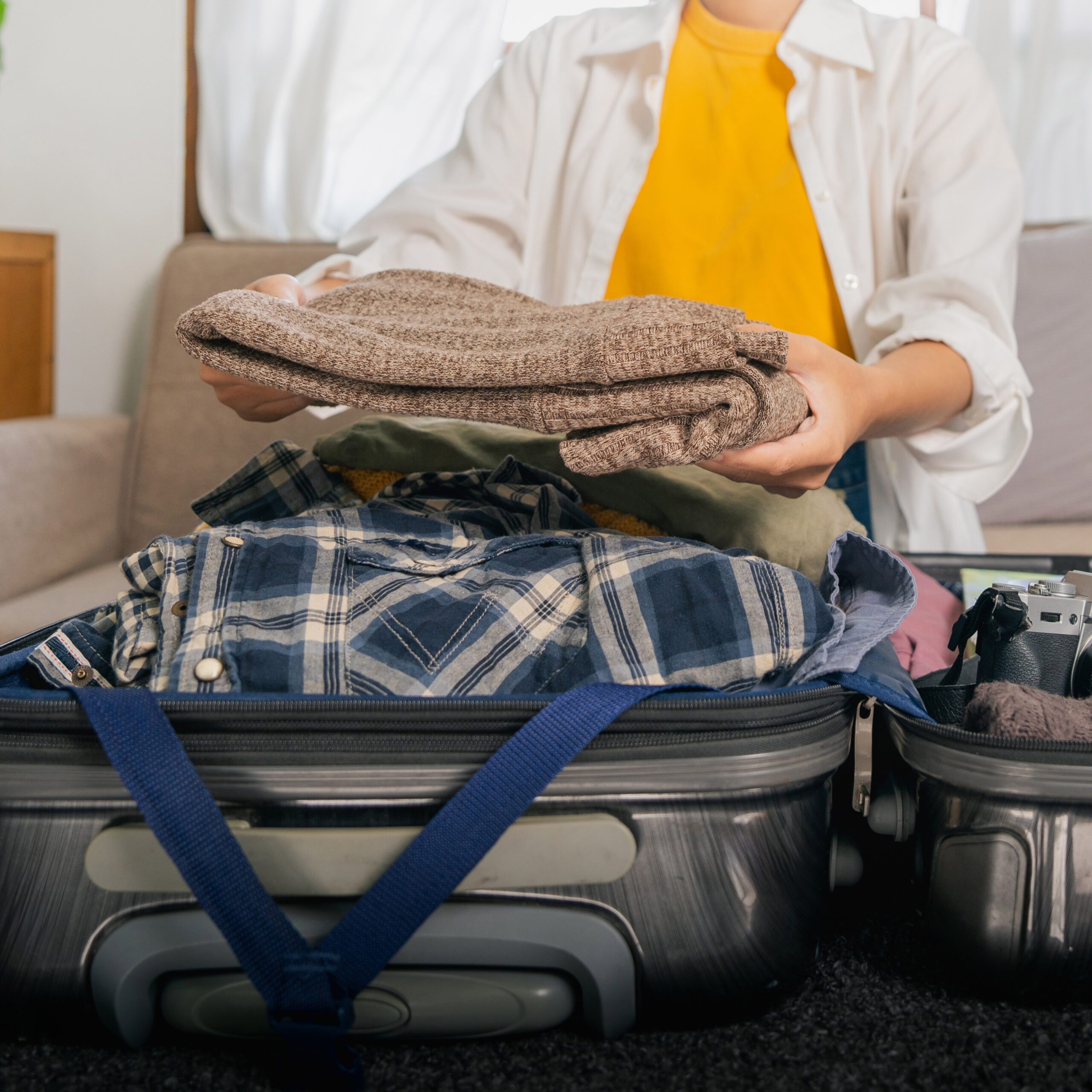 Person packing a suitcase with folded clothes and a plaid shirt for travel