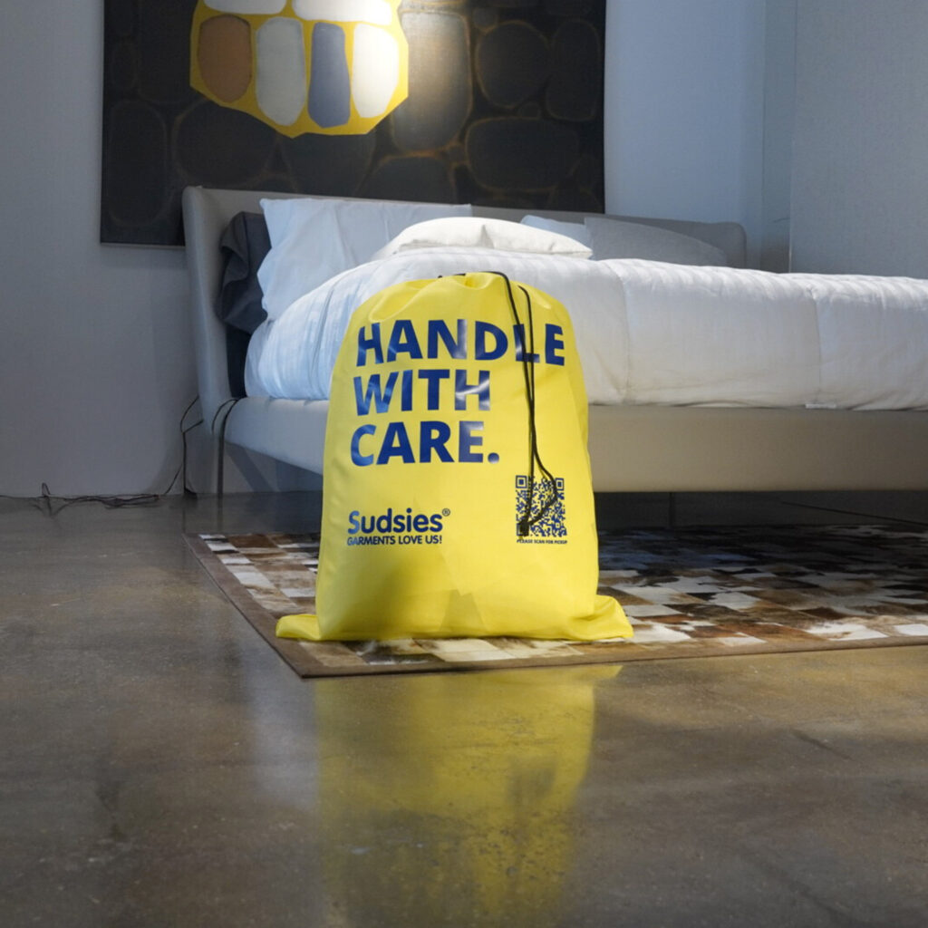 Yellow Sudsies garment bag with “Handle With Care” message in a modern bedroom