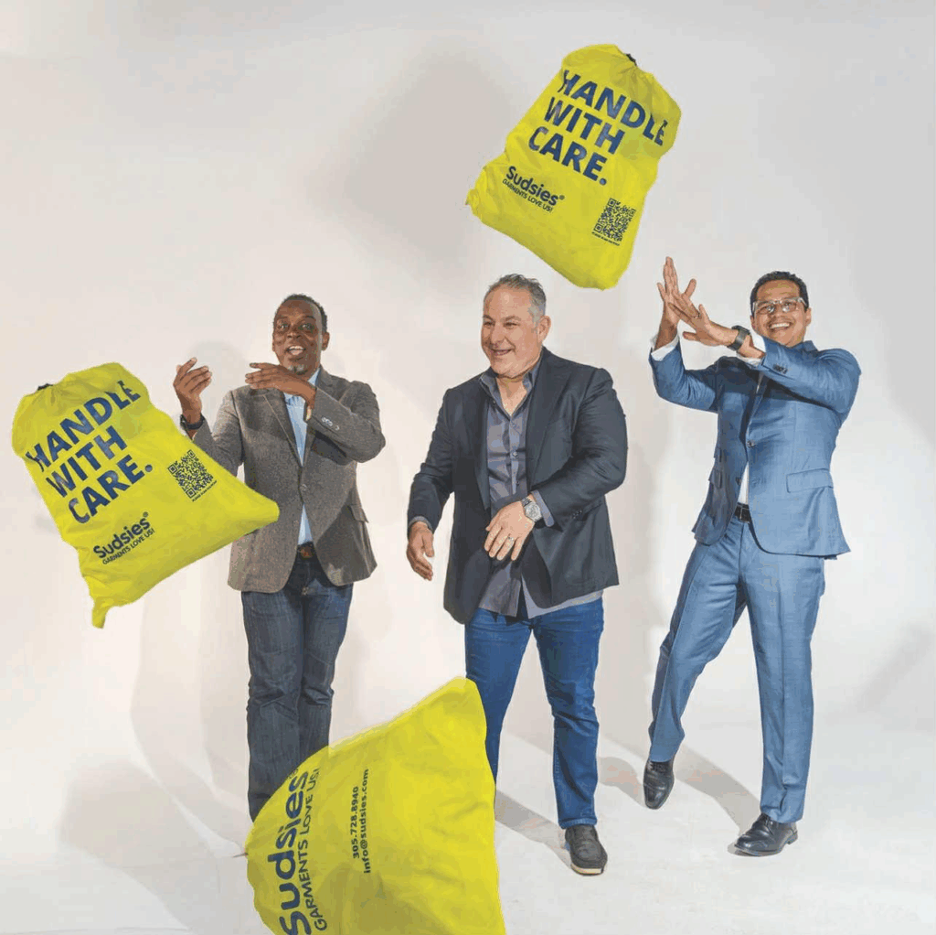 Sudsies team tossing yellow “Handle With Care” garment bags in a studio setting