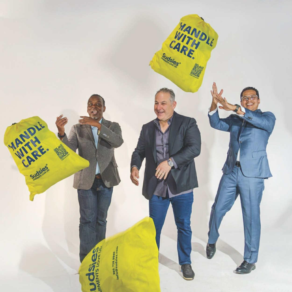 Sudsies team tossing yellow “Handle With Care” garment bags in a studio setting
