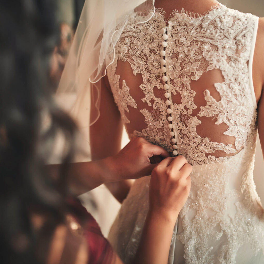 Bridal gown with lace back and covered buttons being fastened during wedding dress fitting
