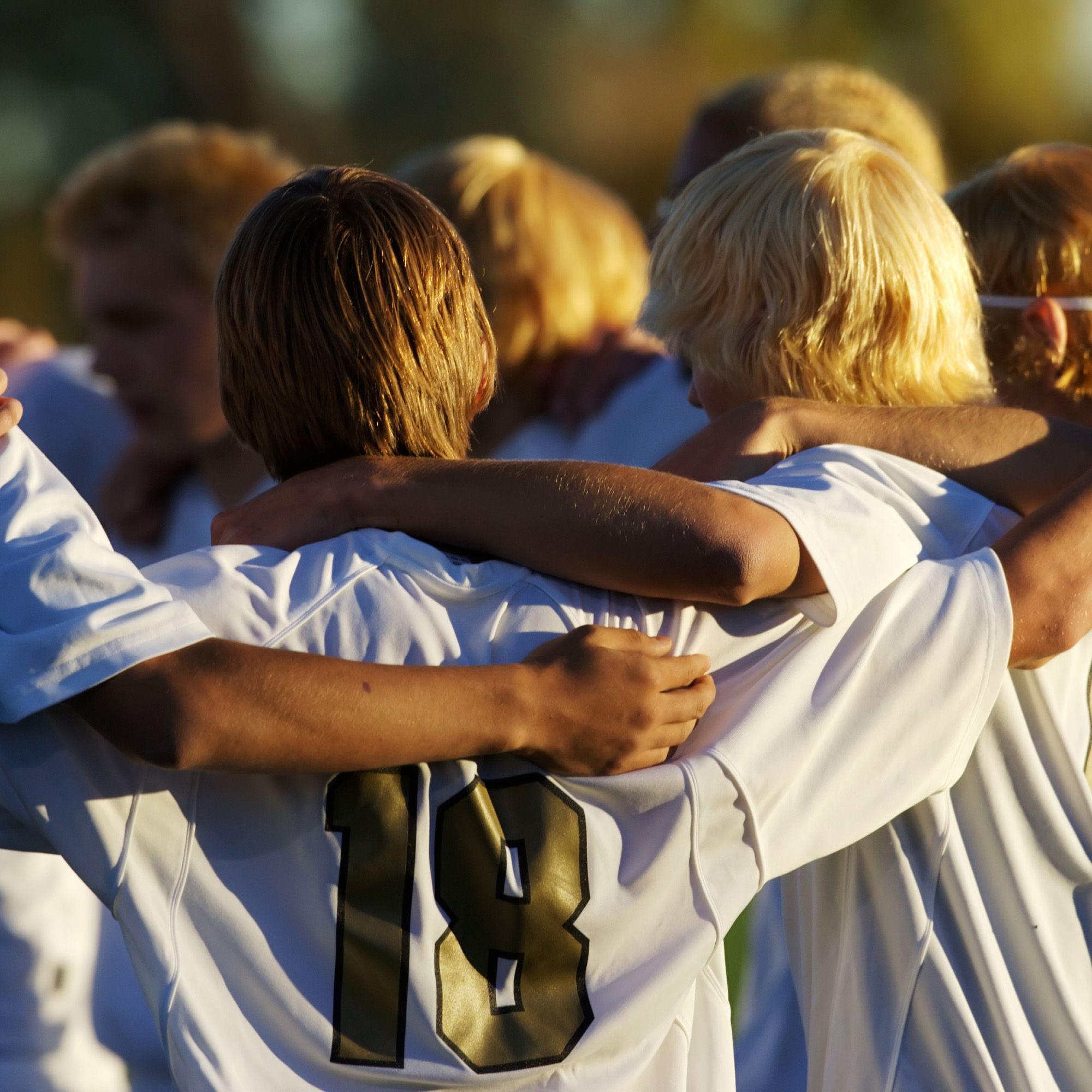 High school athletes in white jerseys with arms around each other in a team huddle