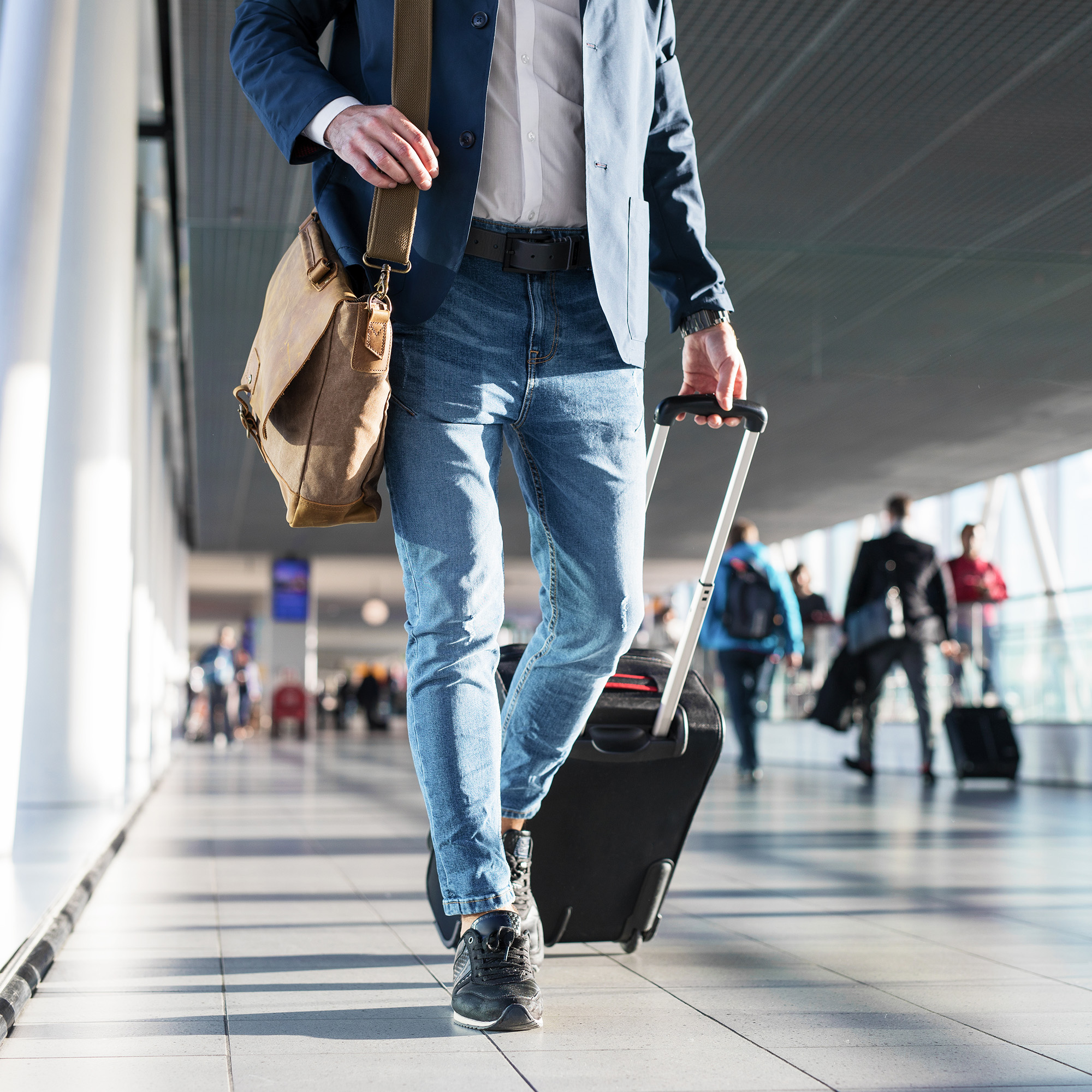 Traveler walking through an airport with a carry-on suitcase and messenger bag
