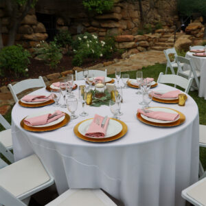 Outdoor event table set with a white tablecloth, pink napkins, and gold charger plates