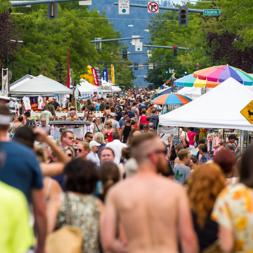 Crowds walking through an outdoor arts festival with colorful tents and vendors
