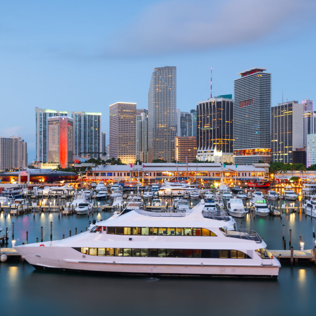Luxury yacht docked at a marina with the downtown Miami skyline at dusk