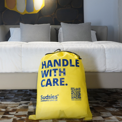 Sudsies Dry Cleaners branded garment bag placed in a luxury bedroom setting