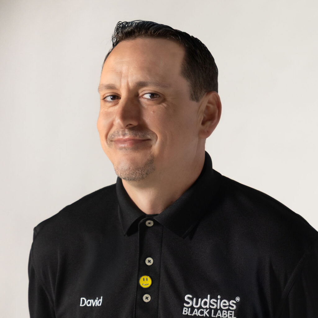 David Zambeli, Manager at Sudsies, wearing a black Sudsies Black Label polo in a professional studio headshot