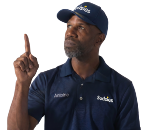 Sudsies garment care valet Antoine wearing a navy branded polo and cap while pointing upward against a transparent background.