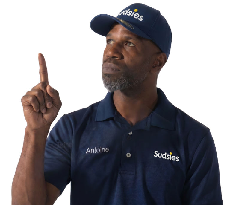 Sudsies garment care valet Antoine wearing a navy branded polo and cap while pointing upward against a transparent background.