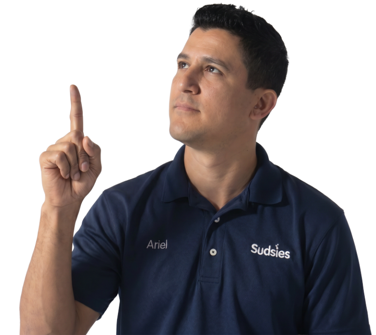 Man wearing a navy Sudsies polo with the name Ariel on the chest, raising his index finger and looking upward.