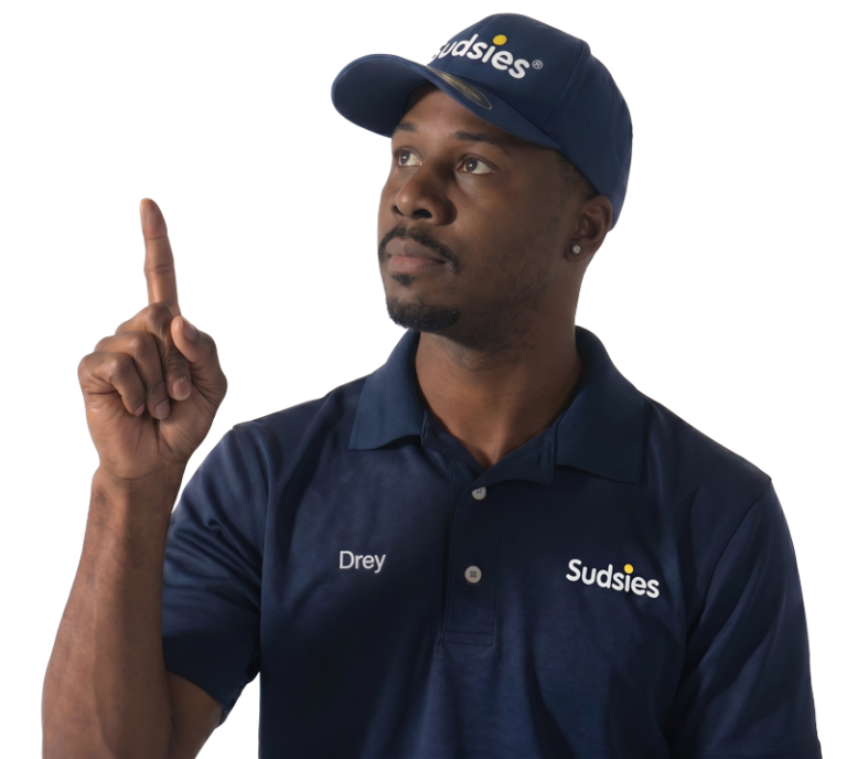 Portrait of a Black man in a navy Sudsies polo with the name'Drey' on it, raising his right index finger.