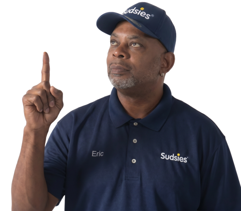 Man wearing a navy Sudsies cap and polo points upward with his index finger.