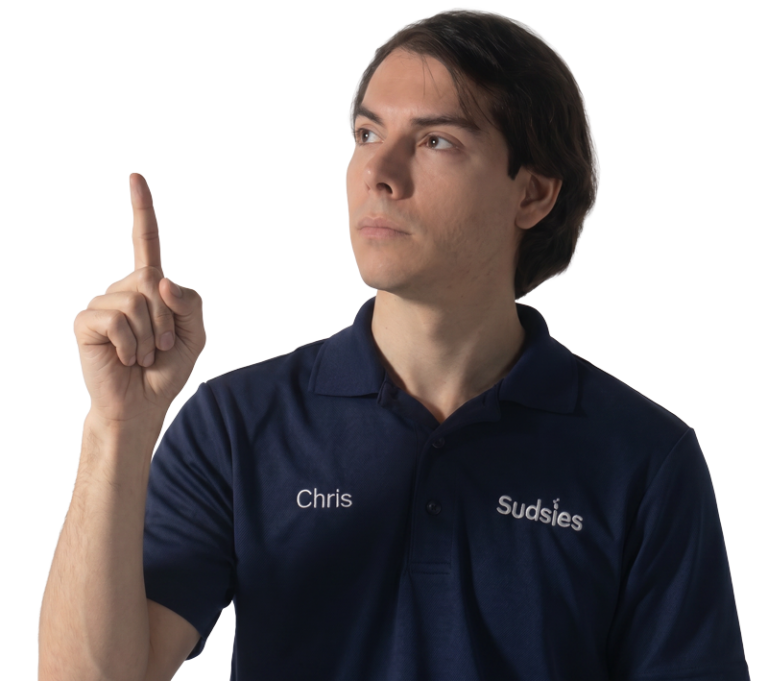 Staff portrait: man in a navy polo marked with'Chris' and 'Sudsies', raising his index finger as if signaling a point.