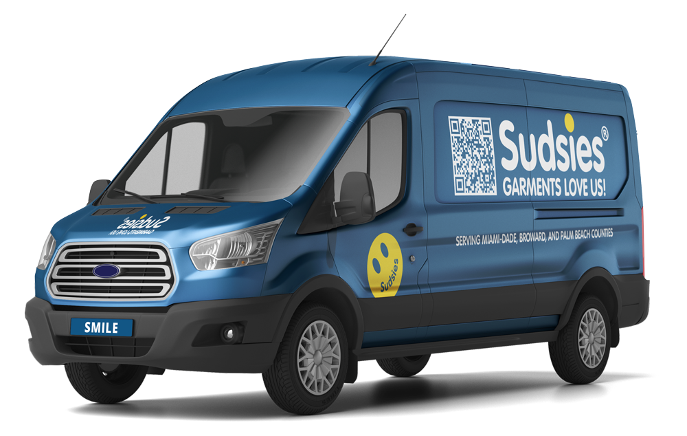 Front three-quarter view of a blue Sudsies pickup and delivery van with branded graphics, QR code, and luxury garment care messaging.