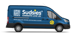 Passenger-side view of a blue Sudsies pickup and delivery van featuring branded graphics, QR code, and South Florida service coverage.
