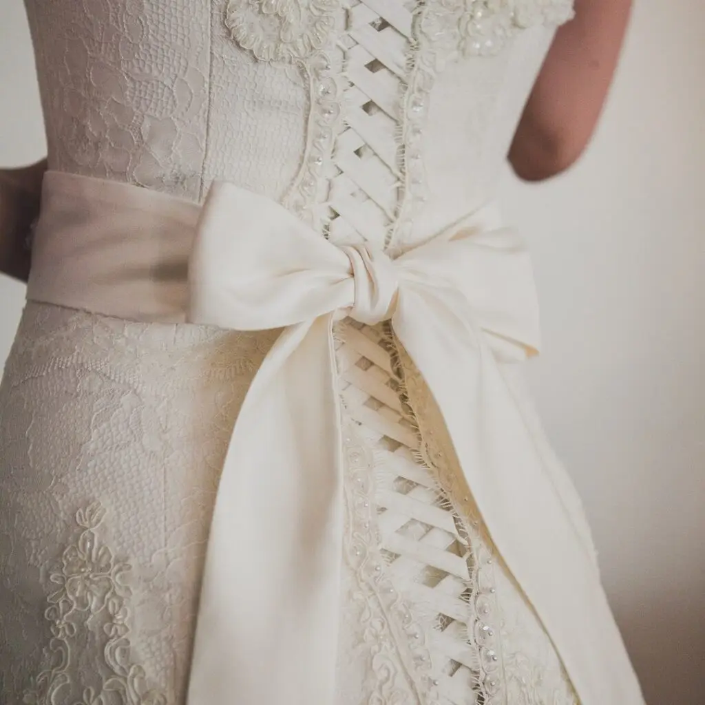 Close-up of the back of an ivory lace wedding dress with corset lacing and a satin bow at the waist.
